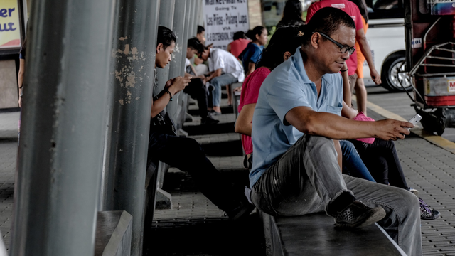 Commuters using mobile devices while waiting for a bus in Manila. Photo by Bloomberg.