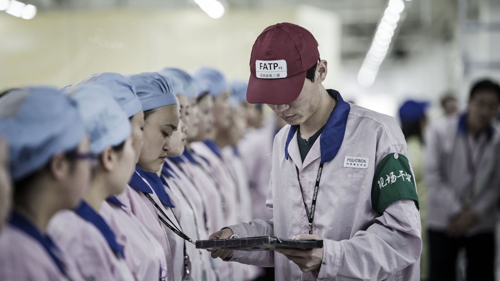 A supervisor holds checks an employee's badge during roll call at a Pegatron factory in Shanghai. Photo by Bloomberg