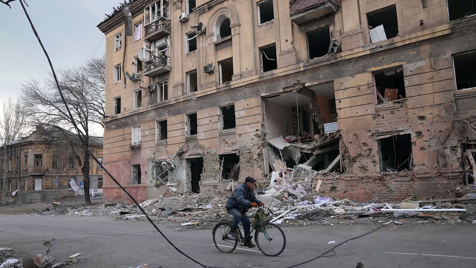 A man rides a bicycle in front of an apartment building that was damaged by shelling in Mariupol, Ukraine. Photo by AP.